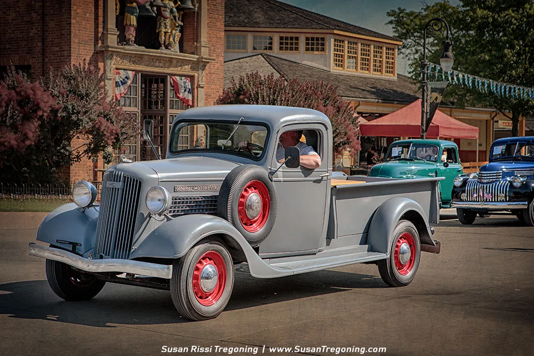 A 1936 GMC T‑14 pickup truck, restored to its original rounded‑fender styling, appears in a vintage parade setting. The truck features classic pre‑war design elements such as a narrow vertical grille, curved hood lines, and exposed headlights mounted on the fenders. Its period‑appropriate wheels and trim emphasize the late‑1930s aesthetic, creating a nostalgic snapshot of early GMC light‑duty truck history.