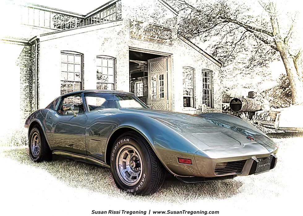 A 1976 silver‑metallic Corvette Stingray sits on a grassy area in front of the historic brick Remington & Sons Blacksmith & Foundry building. The car’s long sculpted hood, sweeping fenders, and Goodyear Eagle ST tires stand out sharply against a partially desaturated background, creating a subtle 3D effect that makes the Corvette appear lifted from the scene. The building’s large windows and industrial signage frame the car.