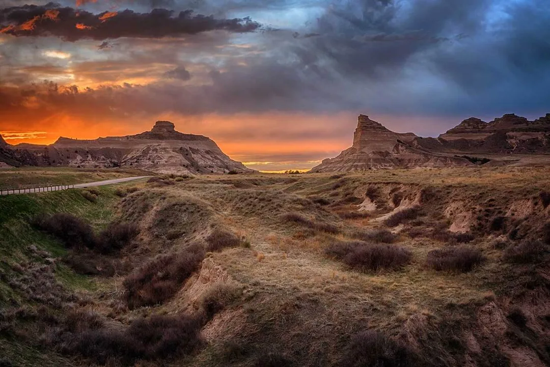 A magnificent sunset colors the sky above Scotts Bluff National Monument in western Nebraska. Sentinel Rock stands on the left and Eagle Rock on the right, two of the bluff’s five formations that rise more than 800 feet above the plains. Mitchell Pass cuts through the center, the historic route many Oregon Trail emigrants used despite its difficult terrain.