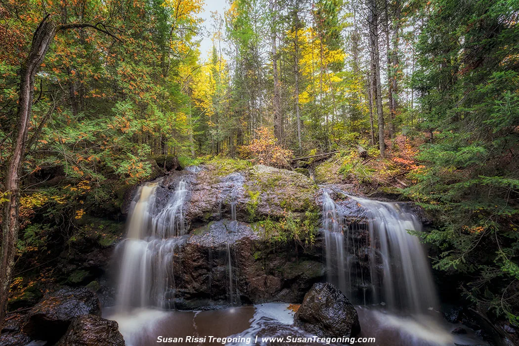 A small waterfall at Now and Then Falls in Amnicon Falls State Park, surrounded by evergreen trees with a light dusting of autumn color.