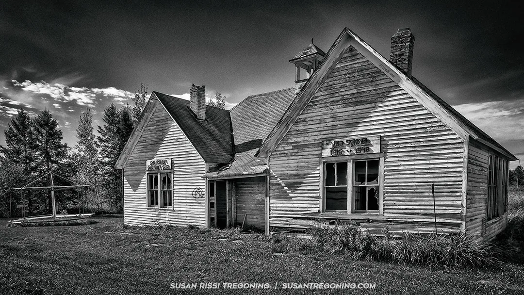 Abandoned two‑room wooden schoolhouse in Cloverland, Wisconsin, with weathered siding and broken windows, standing alone near Highway 13.
