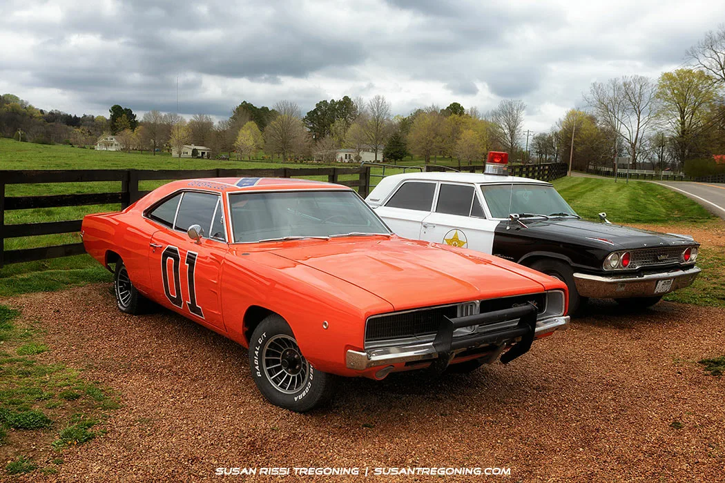 An orange 1969 Dodge Charger known as the General Lee from The Dukes of Hazzard, parked at the town limits, shown with its distinctive “01” door number and roof flag.