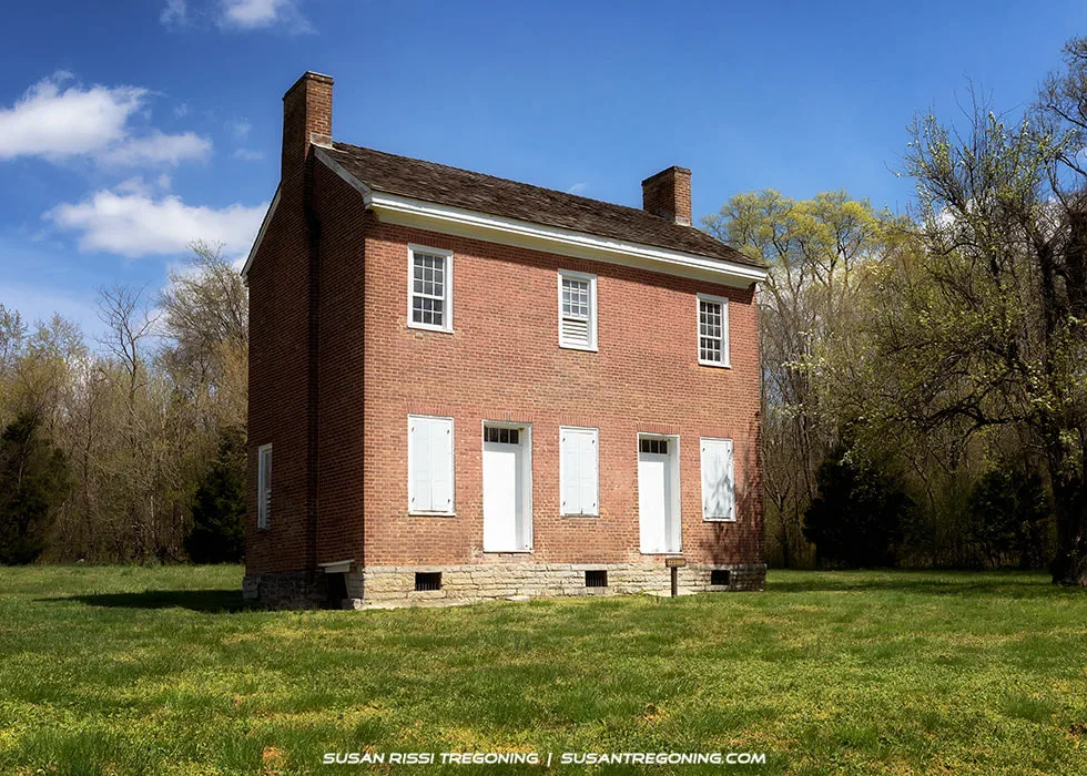 The Gordon House, a two‑story brick home built in 1817–1818, standing beside an open grassy area with trees in the background along the Natchez Trace Parkway.