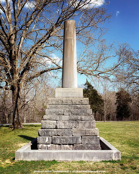 A stone monument with an intentionally broken column marking the gravesite of Meriwether Lewis, set in a grassy clearing surrounded by trees.