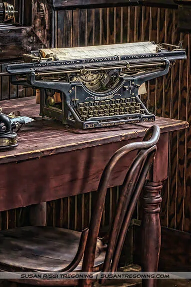 An antique Underwood Standard typewriter sits on a dark wooden desk with a curved wooden chair pulled close. A sheet of paper is rolled into the platen, and the scene is framed by warm wood paneling that gives the workspace a vintage, early‑20th‑century feel.
