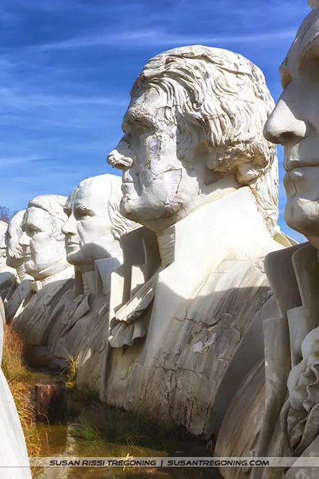 Three large, weathered concrete presidential busts—Thomas Jefferson, James Madison, and Millard Fillmore—stand side by side in an outdoor row under a clear blue sky. Their surfaces show cracks, discoloration, and erosion from years of exposure.