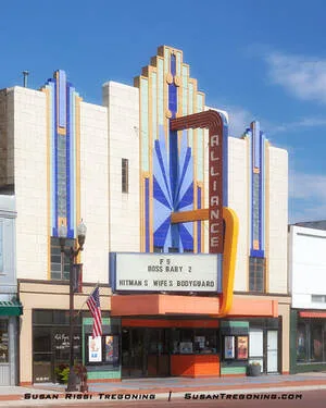 A three‑story Art Deco theater with a tiled facade features its original marquee, box office area, and movie‑poster panels, with modernized entrance doors below.