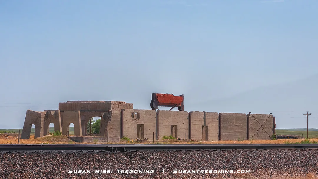 Concrete ruins from an old potash plant stand in an open prairie landscape, with scattered vegetation and rolling hills in the distance.