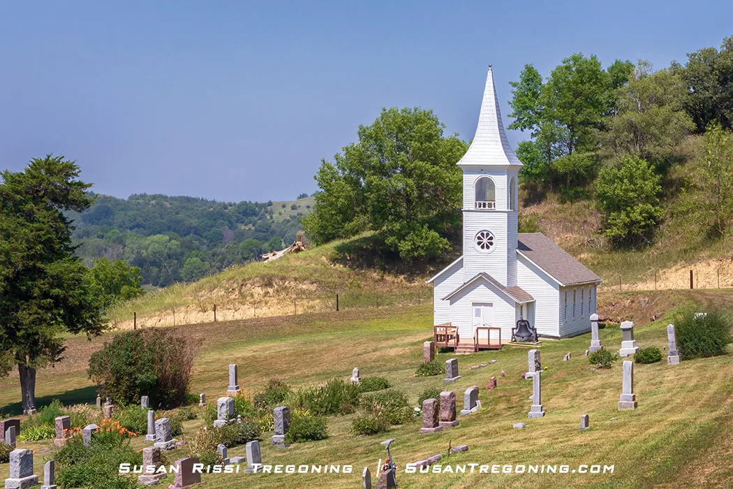 A view of the Ingemann Danish Evangelical Lutheran Church in the Loess Hills near Moorhead, Iowa. A graveyard sits on the church grounds, with headstones arranged in the surrounding rural landscape.