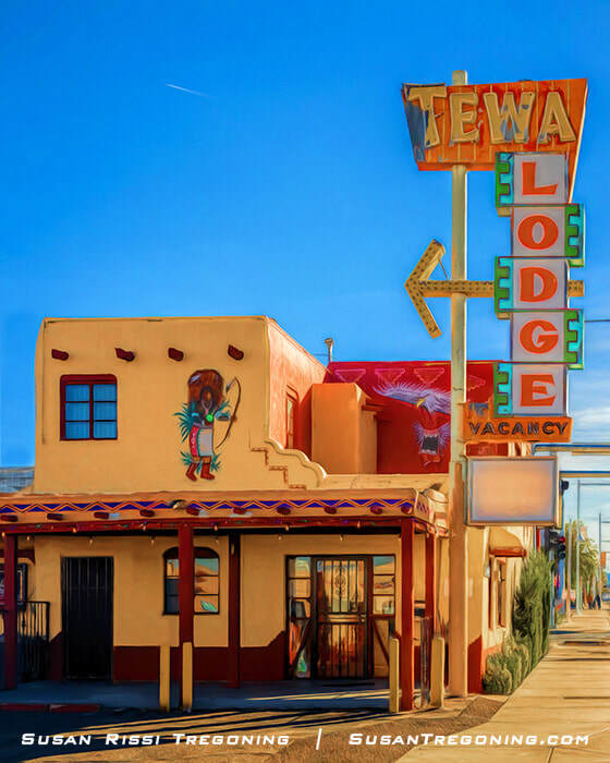 A Pueblo Revival–style motel building in Albuquerque, New Mexico, featuring tan and red stucco walls, exposed wooden beams, and a painted mural of a Native American figure. A large vintage neon sign reading “Tewa Lodge” with “Vacancy” below stands in front of the building. The scene is photographed on a clear, sunny day.