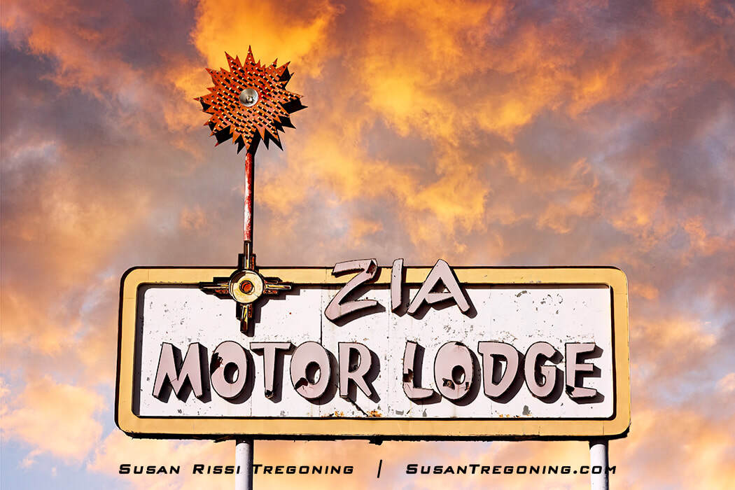 The Zia Motor Lodge neon sign stands alone on a tall metal pole. The vintage sign has a 1960s design with the word “Zia” above a rectangular panel that reads “Motor Lodge.” The surrounding area is open, with sky visible behind the sign.