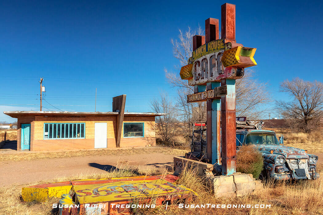  The closed Ranch House Café in Tucumcari, New Mexico, with a weathered building and a tall rusted sign reading “Ranch House Café” and “Mexican Food.” A triangular‑shaped column stands in front of the restaurant, and an old, deteriorated pickup truck sits in the dry grass beside the sign under a clear sky.