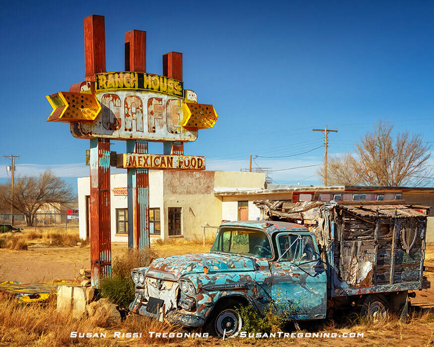 An abandoned, weathered Chevy truck sits in dry grass beside the rusted neon sign for the Ranch House Café in Tucumcari, New Mexico. The sign is faded and mounted on a tall pole, with the vacant café building visible in the background.