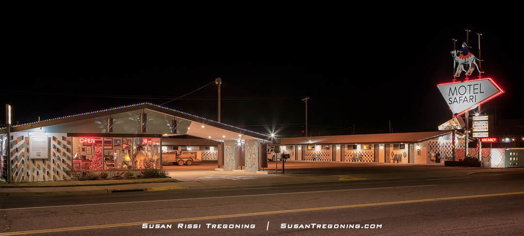 A nighttime view of the Motel Safari in Tucumcari, New Mexico, showing its mid‑century modern façade and brightly lit neon sign with a camel and rider above the words “Motel Safari.” Additional illuminated text advertises amenities, and a classic car is parked under the covered driveway near the office, which has a glowing “Open” sign.