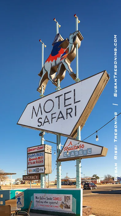 A tall roadside sign for the Motel Safari in Tucumcari, New Mexico, featuring a stylized camel and rider above the words “Motel Safari.” Additional panels advertise amenities, including smart TV and internet, with a smaller sign noting “A Route 66 Classic.” The sign stands against a clear blue sky.