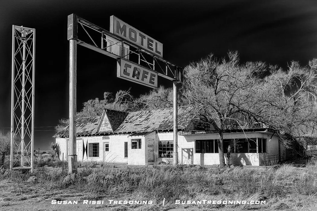 The abandoned State Line Café, Gas Station, and Motel in Glenrio, Texas, with a weathered building showing broken windows, peeling paint, a partially collapsed roof, and a large “Motel” and “Café” sign above the structure, surrounded by dry grass and leafless trees.