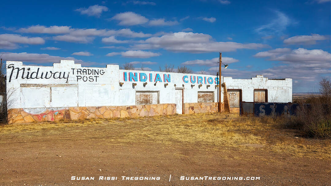 The abandoned Midway Trading Post near Edgewood, New Mexico, with a weathered building showing faded lettering for “Midway Trading Post” and “Indian Curios.” The structure has boarded windows, peeling paint, and a stone lower façade, set in a dry landscape under a partly cloudy sky.