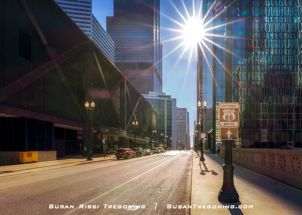     Early morning in downtown Chicago with sunlight across Jackson Boulevard as a Route 66 sign points toward the Adams Street starting point.

