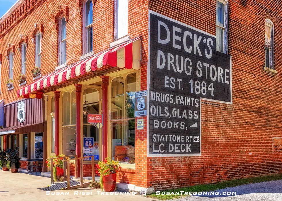 Doc’s Just Off 66 in Girard, Illinois, is shown from the outside. The building features a red and white striped awning and has the Deck’s Drug Store sign painted on the side. The business operates as a restaurant, soda fountain, and pharmacy museum located on Girard’s town square near Illinois Route 4, the 1926 alignment of Route 66.