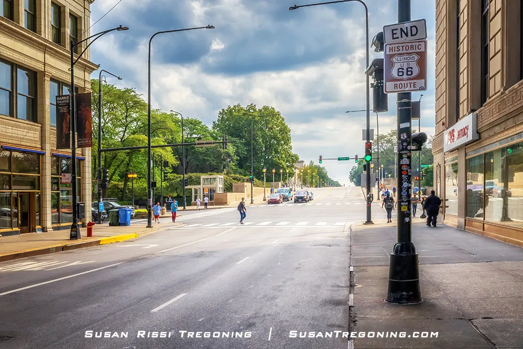 Route 66 End sign on Jackson Boulevard near Michigan Avenue in Chicago, with downtown buildings, pedestrians, and traffic visible at the intersection.