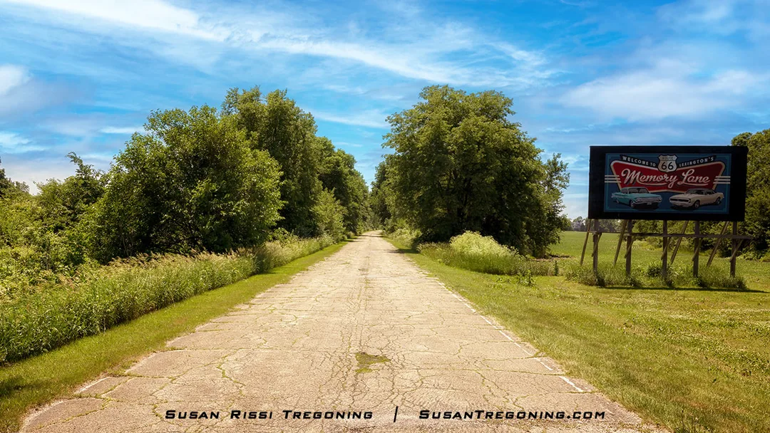 A paved two‑lane road runs through a grassy area with trees under a bright sky. On the right side stands a large sign reading Welcome to Litchfield’s Route 66 Memory Lane with illustrations of two classic cars. The scene shows a preserved stretch of historic Route 66.