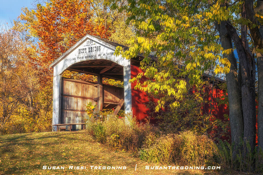 The Neet Covered Bridge, a white-painted Burr Arch truss single‑span bridge, crosses Little Raccoon Creek in Parke County, Indiana. Trees and natural surroundings frame the structure.