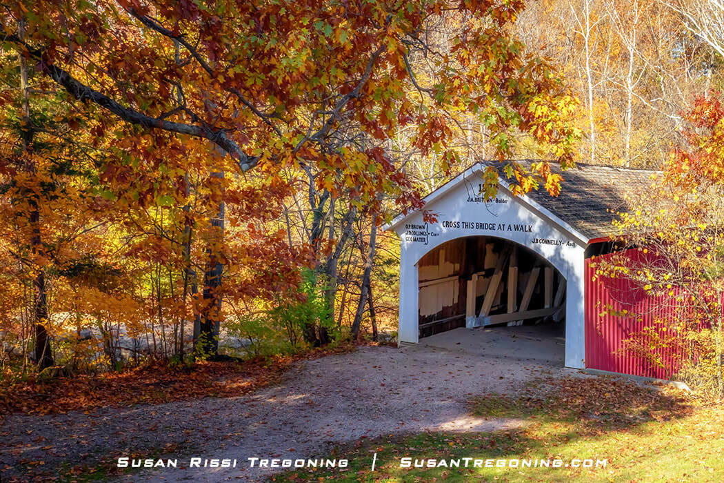 The Narrows Covered Bridge in Turkey Run State Park, with a white front and red sides, set above Sugar Creek and surrounded by bright autumn foliage in shades of yellow, orange, and red.