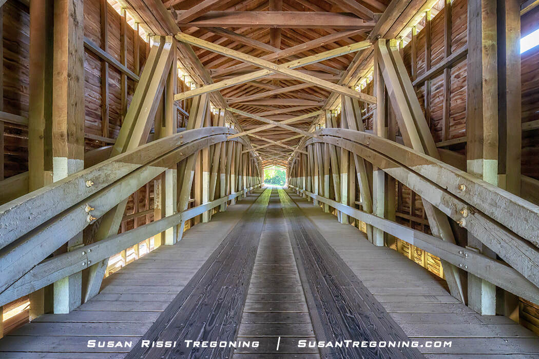  Inside the Jackson Covered Bridge, showing its single‑span structure with double Burr Arch trusses and double King Post elements, with wooden beams and siding visible along the length of the bridge.