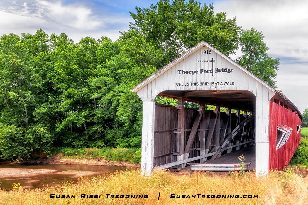 Thorpe Ford Covered Bridge, with a white entrance and red sides, spanning Big Raccoon Creek in Parke County, Indiana, surrounded by green trees and grass.