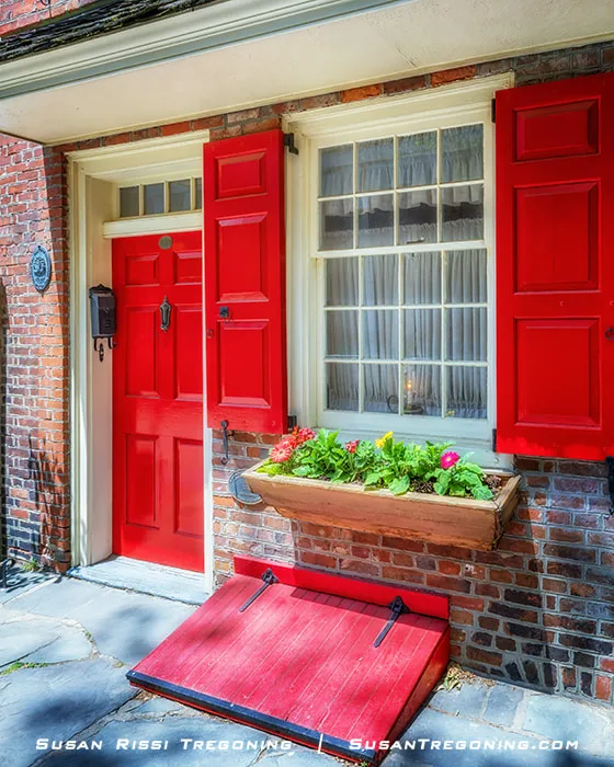 The first home on Elfreths Alley features a red door, matching shutters, and a cellar door, with a candle placed in the window as a welcoming detail.