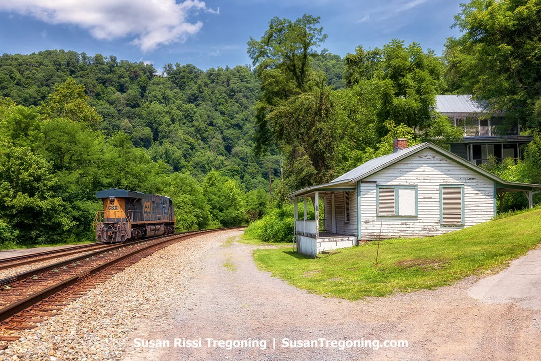 A CSX locomotive idling beside the Marilyn Brown House in Thurmond, West Virginia, a circa‑1900 one‑story, four‑room home that is among the smallest remaining houses in town.
