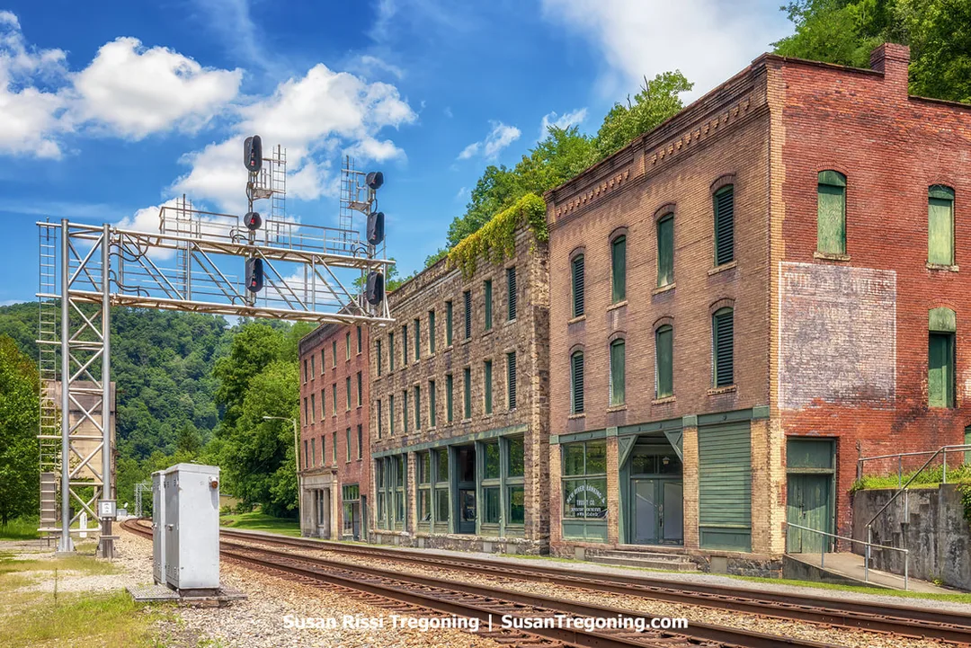 The remaining brick buildings of Commercial Row in Thurmond, West Virginia, standing beside railroad tracks with a metal signal gantry overhead and forested hills in the background.
