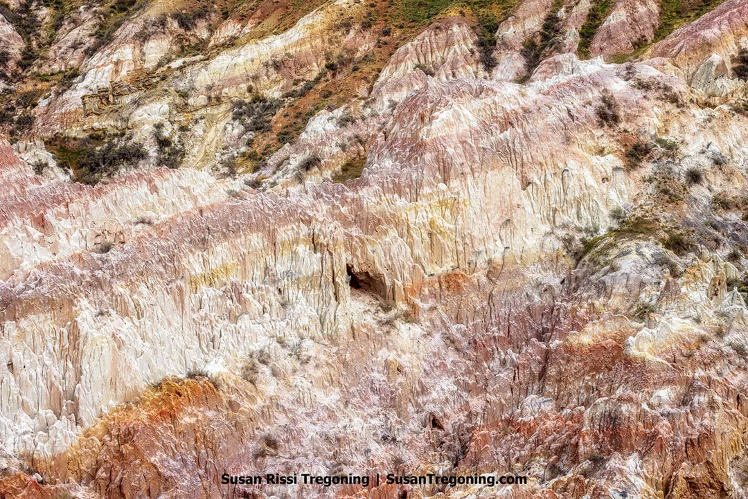 Layered formations of white, pink, red, orange, and brown rock form rugged cliffs and ridges, with sparse vegetation scattered across the colorful badlands terrain.