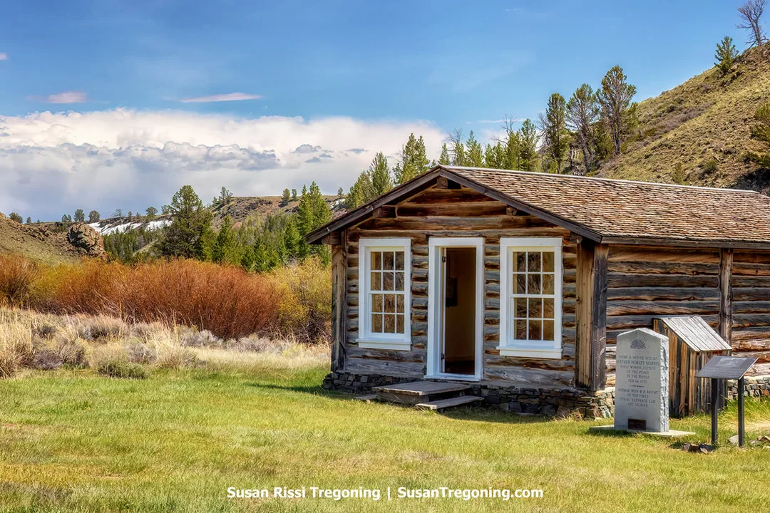 Exterior of the E.A. Slack Cabin in South Pass City, a preserved wooden structure associated with Edward Archibald Slack and his family. The cabin stands among sagebrush and open hills beneath a partly cloudy sky.