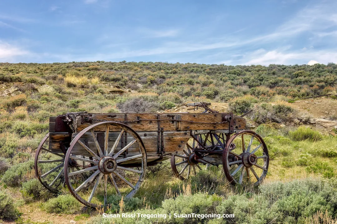 Weathered wooden wagon in the hills above South Pass City, surrounded by sagebrush and set in an open, high‑plains landscape. The bleached wood and worn metal fittings show signs of long exposure to sun and weather.