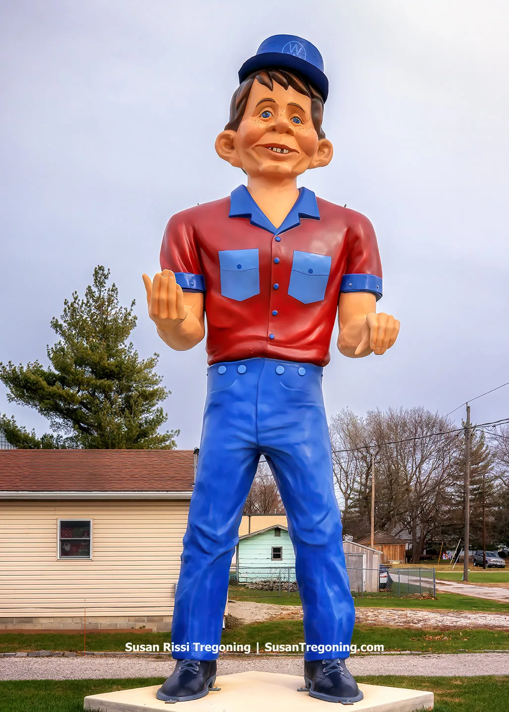 A Muffler Man‑style fiberglass giant known as the Snerd stands outdoors. The figure has a comical grin reminiscent of Alfred E. Neuman from Mad Magazine. It was likely produced between 1966 and 1970 and shows evidence of past damage and repair, including missing or replaced sections. The giant is associated with earlier uses at a miniature golf course, a hot dog stand, and later the Wagon Wheel Bar in Madison, Ohio.