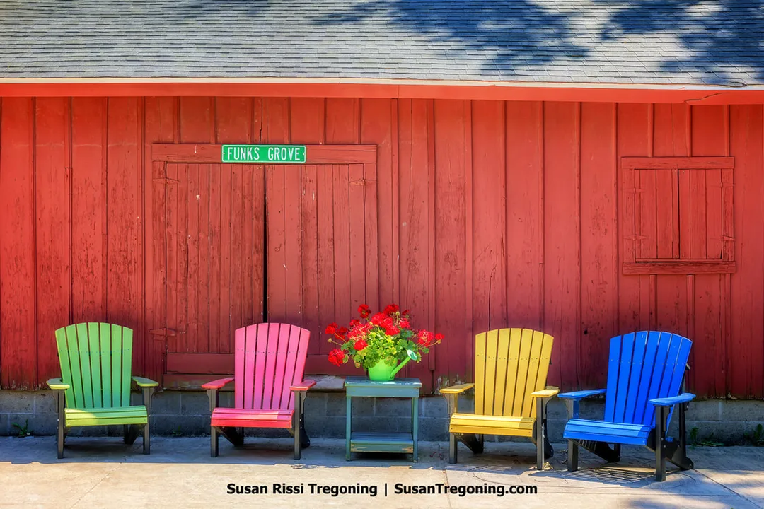 Four brightly colored Adirondack chairs are arranged in front of the original red Funks Grove Depot, which was moved to the Funks Grove Maple Sirup Farm grounds from its previous location. The depot stands along historic Route 66 in Shirley, Illinois.