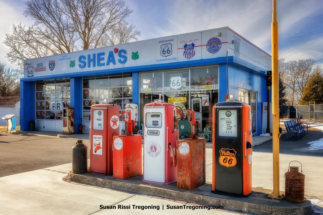 Shea’s Gas Station on Route 66 in Springfield, Illinois, is shown as a blue and white building with a collection of old gas pumps displayed out front. The structure previously operated as a Marathon station from 1955 to 1982 before becoming Shea’s Gas Station Museum.