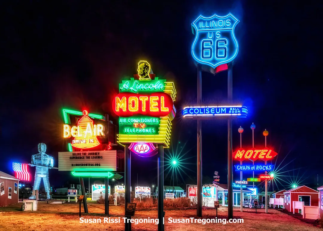 The Legends Neon Park signs are illuminated at night at the Route 66 Experience on the Illinois State Fairgrounds in Springfield, Illinois. The display features recreated neon signs from the Bel Air Drive‑In, A. Lincoln Motel, Coliseum Ballroom, and Chain of Rocks Motel, along with a tribute to the muffler men associated with Route 66.