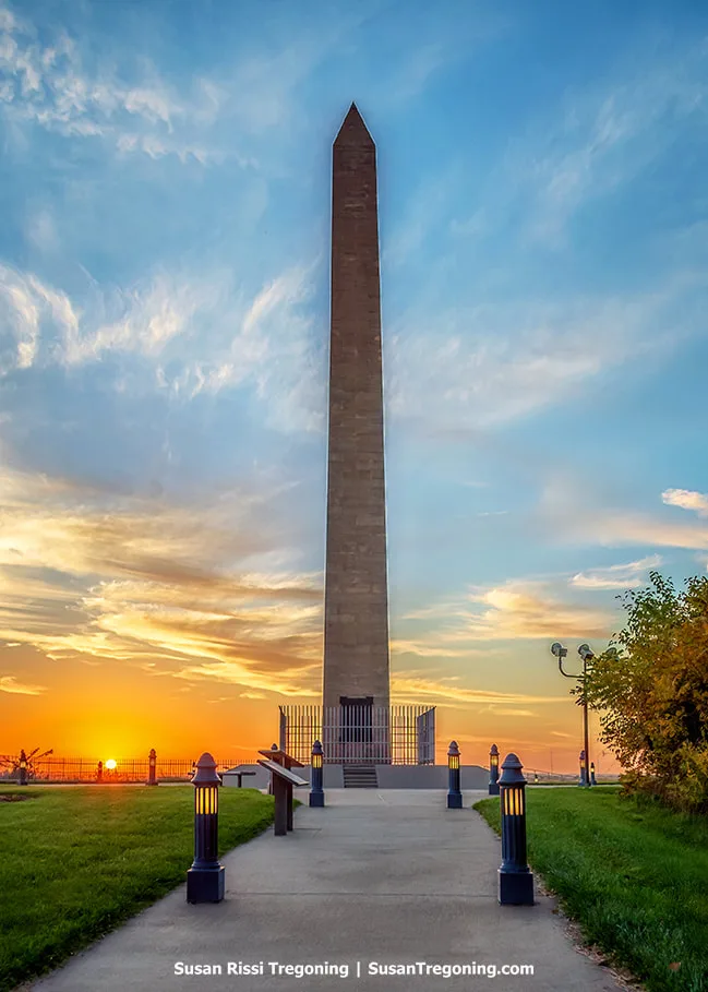 A view of the Sergeant Floyd Monument at sunset. The tall obelisk appears in shadow, with the sky showing sunset colors behind it but no direct sunlight on the monument.