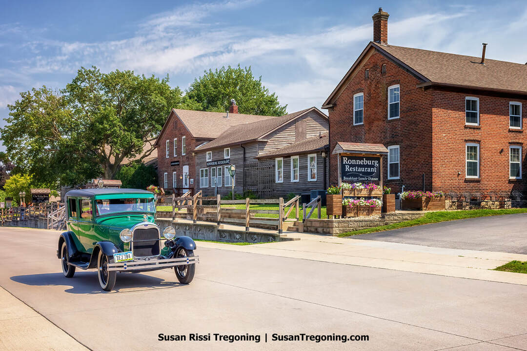 A green Ford Model A cruises past the red brick and natural wood sided Ronneburg Restaurant as the Iowa Model A Car Show concludes in Amana, Iowa.