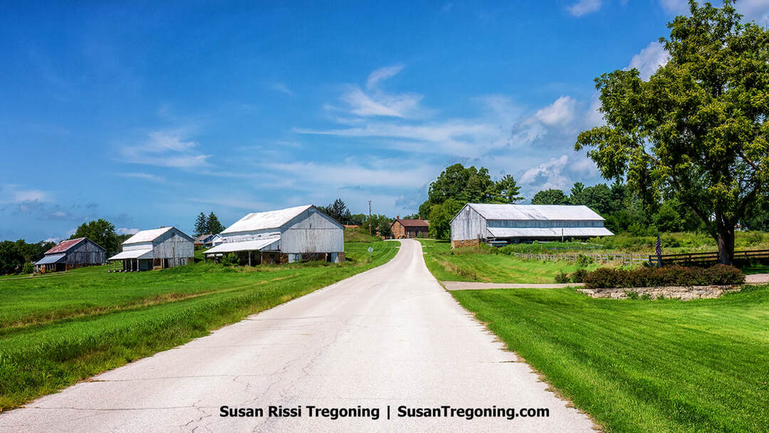A road passes between a grouping of historic barns at the edge of West Amana in Iowa’s Amana Colonies.