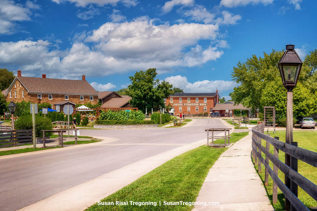 The Mill Area in the Amana Colonies, Iowa. Facing north along 48th Avenue in Amana, Iowa, you can see the Blumen Haus florist and the Amana Furniture Shop on the curve. This section of the Amana Colonies used to be a bustling industrial hub, home to the train depot and several mills. Today, only the Amana Woolen Mill and the Amana Furniture Shop, which occupies part of the old Amana Calico Mill, stand as reminders of that era.