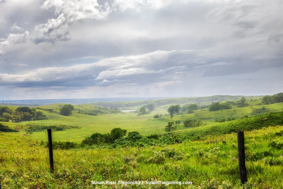A view down into Broken Kettle Grassland Preserve from Butcher Road during a fast‑moving summer rainstorm. Low clouds and rain soften the rolling Loess Hills, with the open grassland slopes fading into the mist.