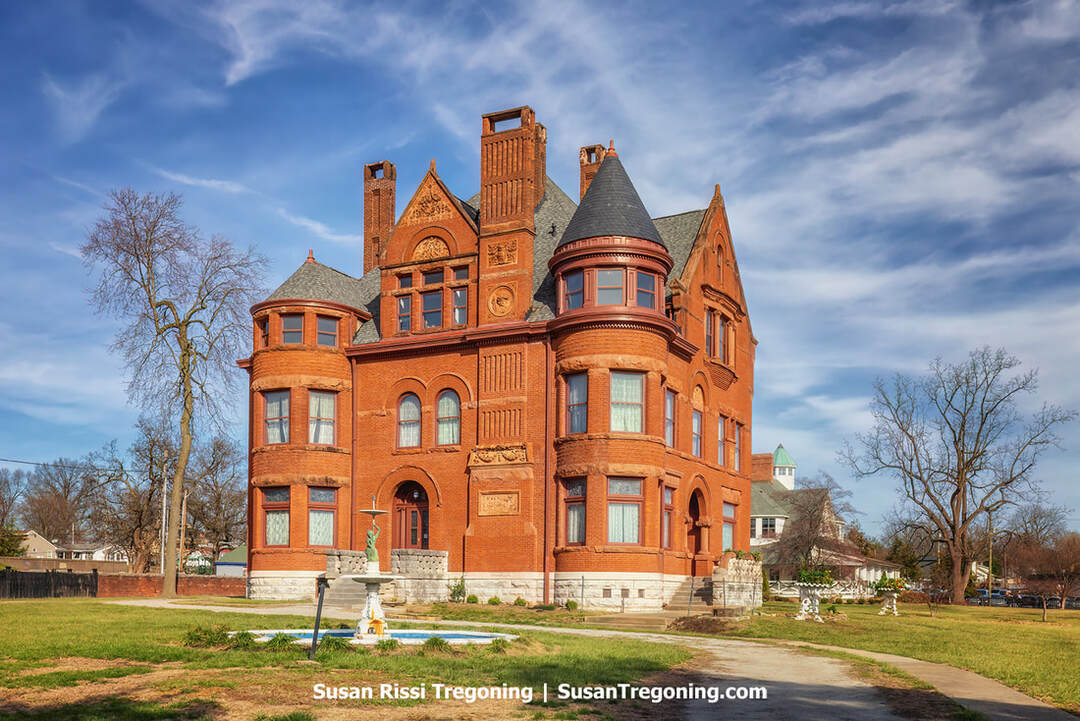 The Howard Steamboat Museum, a grand Victorian mansion with ornate architectural details, stands behind a manicured lawn and walkway. The red‑brick home features decorative trim, arched windows, and a prominent tower, reflecting the opulent style of the Howard family who built and operated the famed Howard Shipyard.