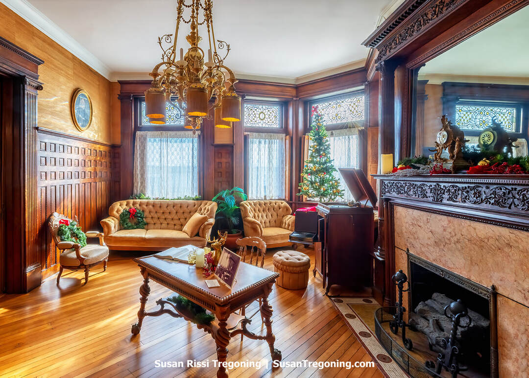 The library inside the Howard Steamboat Museum features dark wood bookcases filled with vintage volumes, ornate carved trim, and period Victorian furnishings. A large wooden desk and upholstered chairs sit within the richly detailed room, reflecting the Howard family’s refined taste and the craftsmanship of the steamboat‑building era.