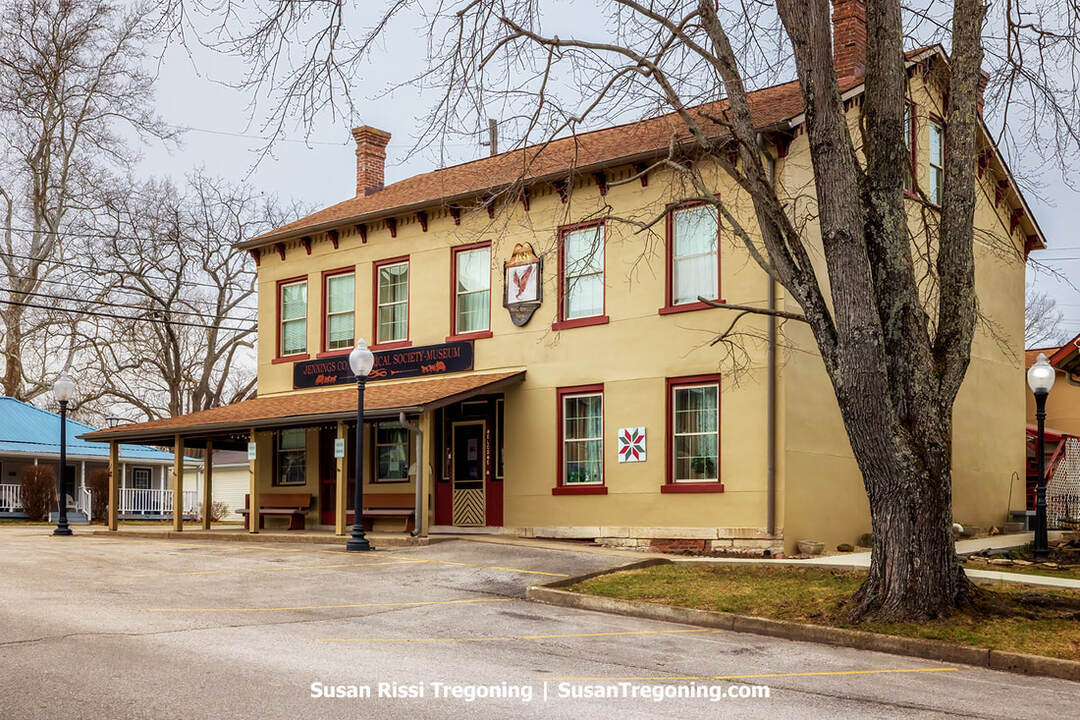 The North American House in Vernon, Indiana, a historic gold colored building with a covered front porch and Jennings County Historical Society signage, shown from the street.