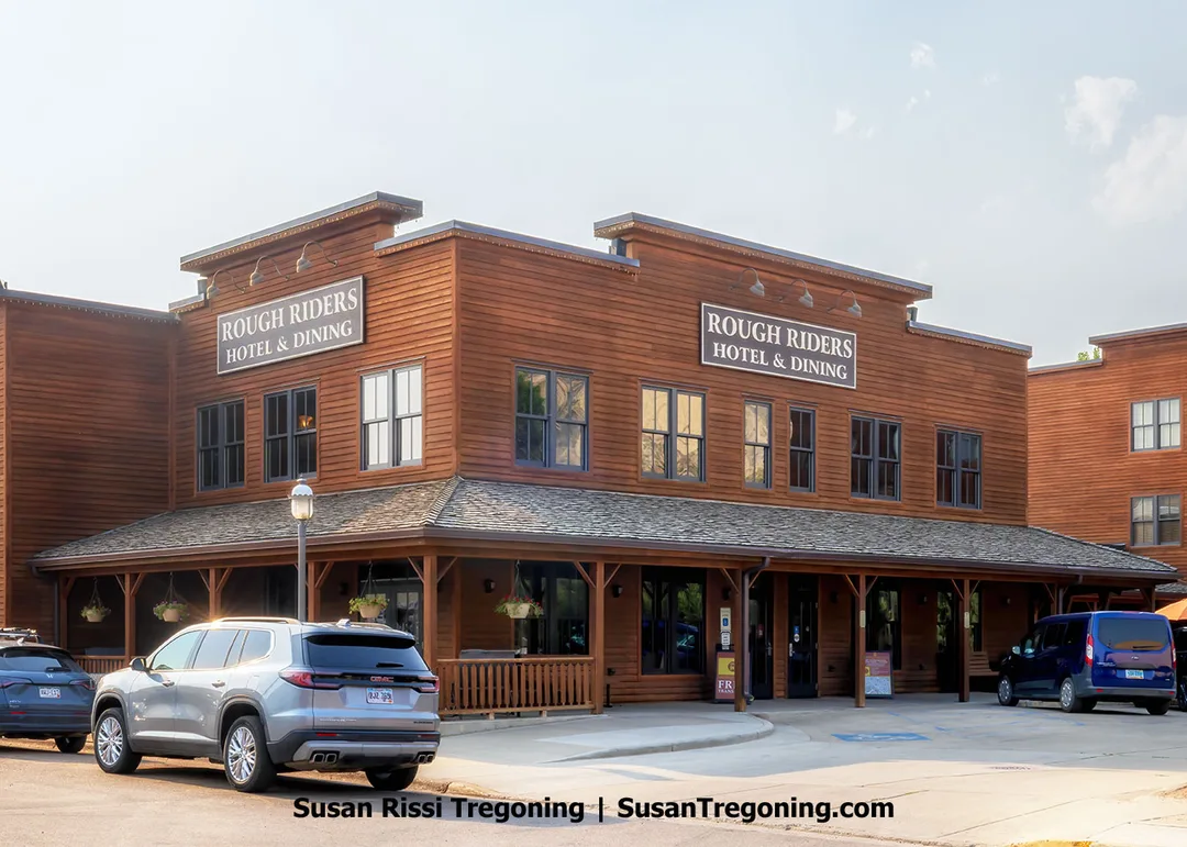 The Rough Riders Hotel in Medora, North Dakota, features a classic Western‑style wooden facade with large windows and a covered porch. Originally built in 1884 as the Metropolitan Hotel, it now stands as a restored landmark honoring Theodore Roosevelt’s legacy and Medora’s frontier heritage.