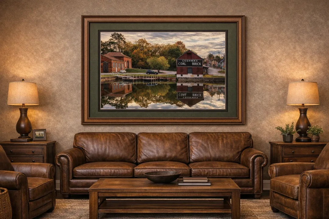 Two historic brick buildings, including Cushwa’s Coal Brick, reflect in the still canal water under a partly cloudy morning sky, with autumn trees and houses in the background.