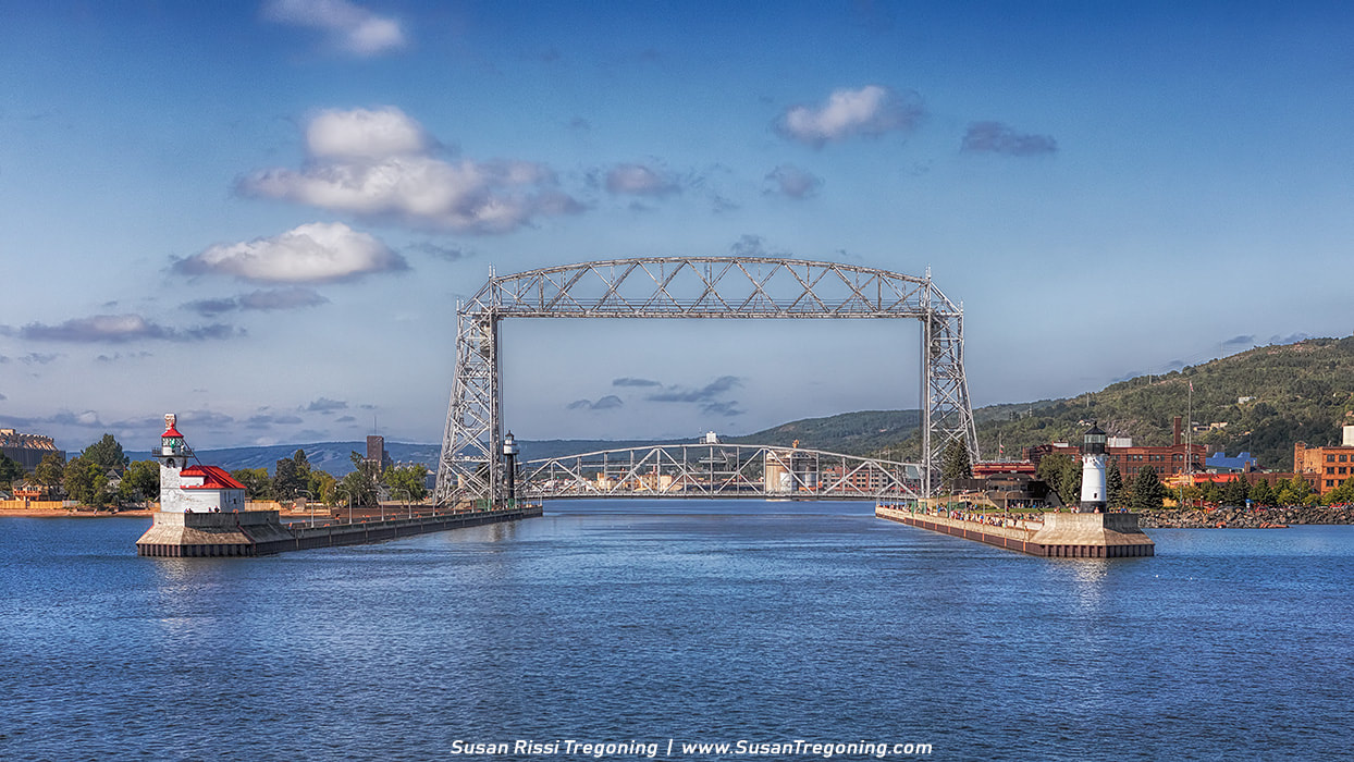 The view of the Aerial Lift Bridge and the canal pier’s lighthouses as we enter the Duluth Ship Canal from Lake Superior. The Duluth Ship Canal is an artificial channel cut through Minnesota Point, providing direct access to Duluth harbor from Lake Superior. This channel is defined by a pair of breakwaters 1,720 feet long and 300 feet apart. The piers project roughly 1,150 feet beyond the shoreline and the channel is maintained at 245 feet wide and 28 feet LWD, allowing passage of ocean-going ships. Three lighthouses are placed on the sides of the channel: the Duluth North Pier Light and the Duluth South Breakwater Outer Light mark the lake ends of the channel, while the Duluth South Breakwater Inner Light functions with the south breakwater light as a range light. At the harbor end, the channel is straddled by the Aerial Lift Bridge which connects Minnesota Point to the rest of the city. There are no locks; most ships transit the channel under their own power, though tug service is available in case of adverse weather. Around a thousand vessels a year ship from the Duluth–Superior port. 